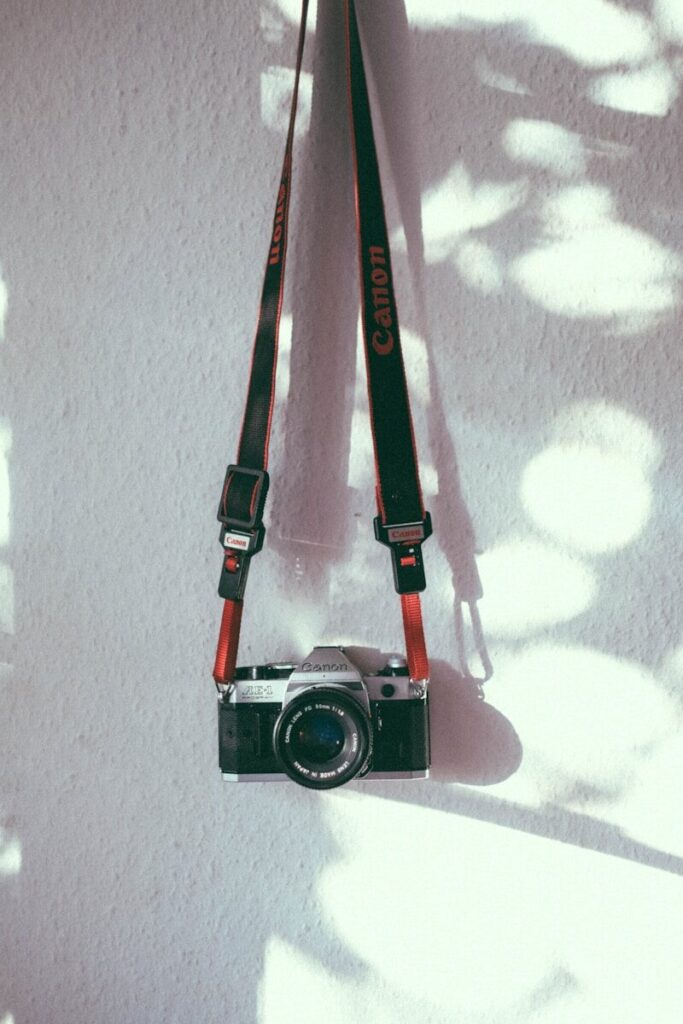 Vintage canon film camera hanging against a sunlit white wall.